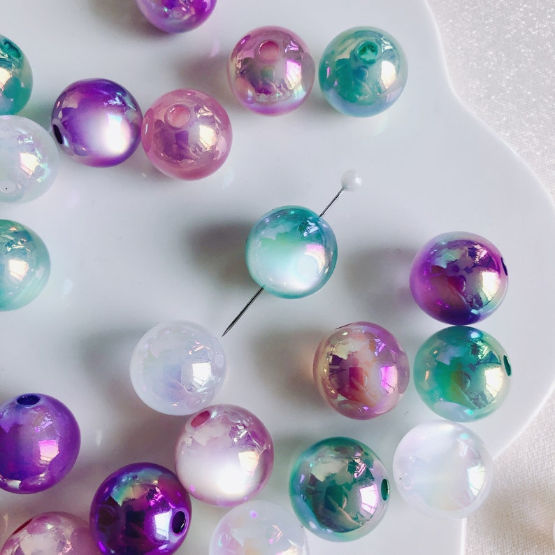 May include: Assortment of iridescent round beads in various shades of pink, purple, blue, and green. The beads have a pearlescent finish and are perfect for crafting jewelry or other decorative projects.
