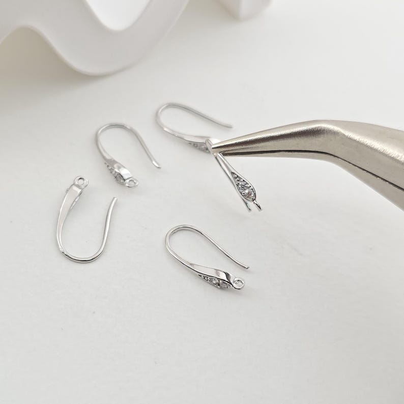 May include: Four silver earring hooks with clear crystal accents. The hooks are designed to be used for jewelry making.