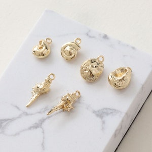 Può includere: Sei ciondoli a forma di conchiglia dorati con un anello per attaccarli a gioielli o altri oggetti artigianali.