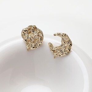 May include: A pair of gold-tone earrings with a textured, irregular shape. One earring is a circle and the other is a crescent moon.