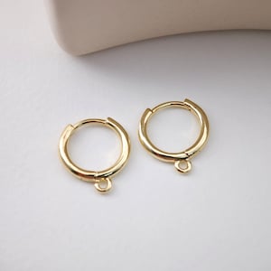 May include: A pair of gold hoop earrings with a small jump ring hanging from each hoop.