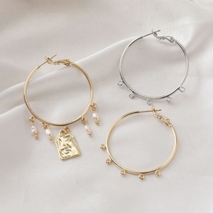 Könnte beinhalten: Drei Paar Creolen, ein Paar ist silberfarben mit einem schlichten Design, die anderen beiden Paare sind golden, eines mit einem kleinen rechteckigen Anhänger und das andere mit kleinen Perlenakzenten.