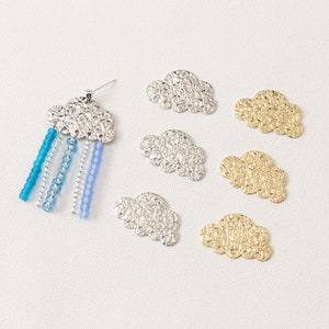 May include: Six metal cloud charms, two gold and four silver, with a textured surface. One silver cloud charm is attached to a beaded earring.