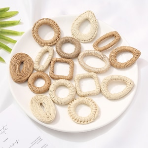 May include: A collection of woven raffia shapes in various forms, including circles, ovals, and squares. The natural beige and tan tones of the raffia create a rustic, handmade aesthetic. The shapes are arranged on a white plate.