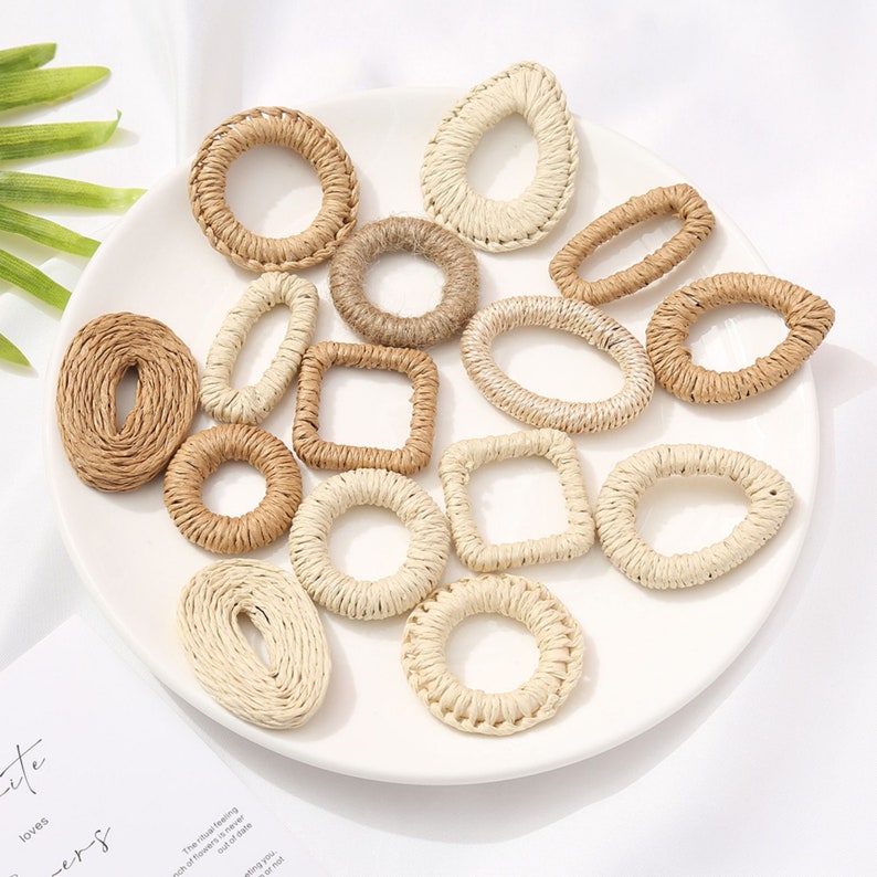 May include: A collection of woven raffia shapes in various forms, including circles, ovals, and squares. The natural beige and tan tones of the raffia create a rustic, handmade aesthetic. The shapes are arranged on a white plate.