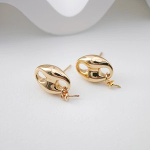 May include: A pair of gold-toned earrings with a unique oval shape and a small loop on the bottom. The earrings are on a white background.
