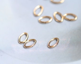 May include: A close-up of a group of gold oval jump rings. The rings are scattered on a light blue surface.