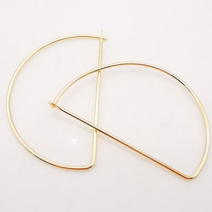 Pode incluir: Um par de brincos de argola de ouro com um design geométrico único. Os brincos são feitos de metal fino e têm uma forma semicircular.