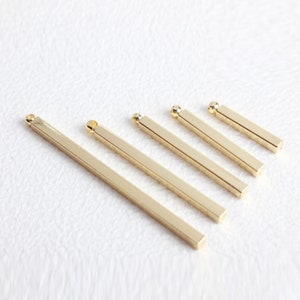 May include: Set of six gold-toned metal bar pendants with a loop at the top. The bars are different lengths, ranging from about 2.5 cm to 7.5 cm.