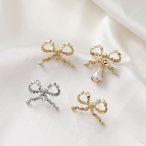 May include: Four gold and silver bow-shaped earrings with a pearl drop on one of the gold earrings.