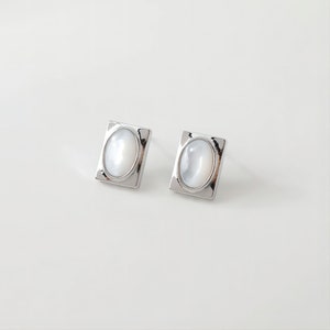 May include: A pair of silver earrings with oval-shaped white mother-of-pearl stones set in square frames.