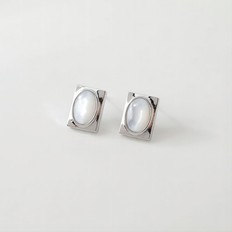 May include: A pair of silver earrings with oval-shaped white mother-of-pearl stones set in square frames.