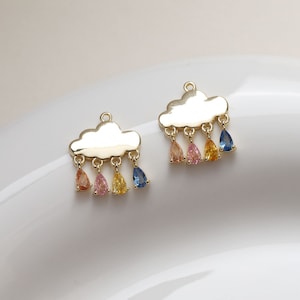May include: Two gold-tone cloud charms with dangling teardrop-shaped crystals in shades of blue, pink and yellow.