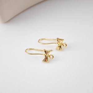 May include: A pair of gold-toned earring findings with a bow shape. The findings have a loop at the top for attaching to earrings.
