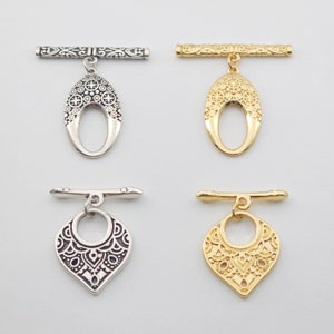 May include: Four ornate metal toggle clasps, two in silver and two in gold. Each clasp features a decorative bar and a dangling pendant with an intricate design.