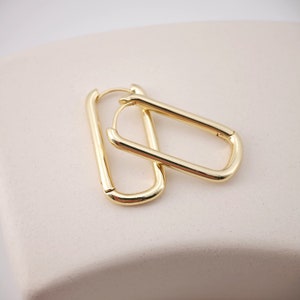 Op de afbeelding: Een paar goudkleurige rechthoekige oorringen. De oorbellen hebben een gepolijste afwerking en een eenvoudig, modern design. De ringen zijn licht afgerond op de hoeken en hebben een veilige sluiting.