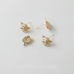 Op de afbeelding: Een paar gouden oorbel studs met een kattengezicht. De oorbellen worden getoond op een witte achtergrond.