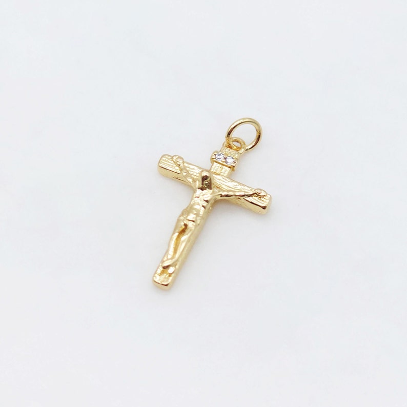 May include: A gold-toned crucifix pendant with a small, clear stone at the top. The crucifix features a detailed depiction of Jesus Christ.