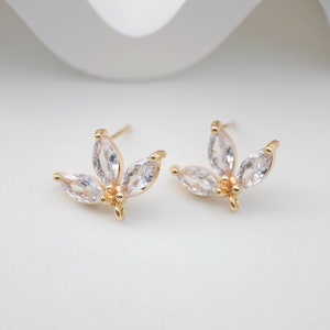 May include: A pair of gold earrings with a delicate design featuring five clear, marquise-shaped stones. The stones are arranged in a flower-like pattern.