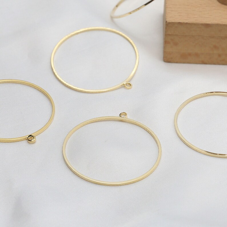 May include: Four gold-colored metal hoops with a small loop at the bottom. The hoops are on a white fabric surface.