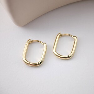 Puede incluir: Un par de pendientes de aro cuadrados de color dorado. Los pendientes son simples y minimalistas en diseño.