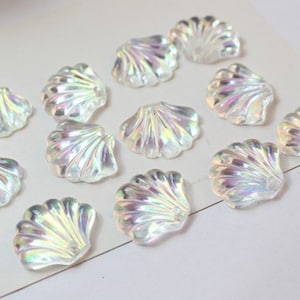 May include: A collection of iridescent white seashell-shaped embellishments. The shells are made of plastic and have a pearlescent finish.