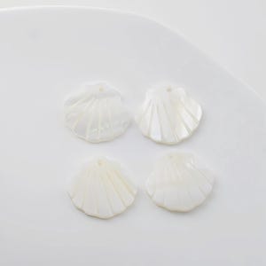 Peut inclure: Quatre perles blanches en forme de coquille avec un trou au centre. Les perles sont lisses et ont une finition naturelle et irisée.