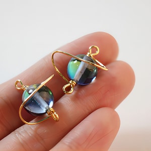 May include: Two gold wire wrapped iridescent glass beads with a blue, green, and purple color shift. The beads are attached to gold jump rings.