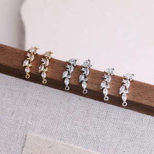 May include: Three pairs of metal earring connectors featuring marquise-cut and round-cut clear cubic zirconia stones arranged in a leaf-like cluster. One pair is gold-toned, and two pairs are silver-toned, each with a small loop at the bottom.