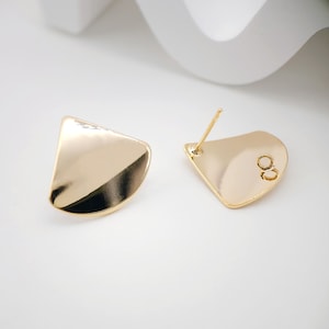 Może przedstawiać: Para złotych kolczyków w kształcie zakrzywionego trójkąta. Kolczyki są proste i nowoczesne.