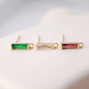 Peut inclure: Trois boucles d'oreilles en forme de barre dorées avec des pierres de différentes couleurs. Les boucles d'oreilles ont une petite boucle en haut et un long axe pour le perçage. Les pierres sont vertes, claires et roses.