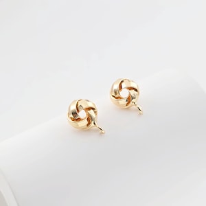 Puede incluir: Un par de pendientes de nudo de color dorado con un diseño sencillo.