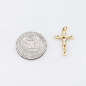 May include: A gold-tone crucifix pendant with a small clear stone at the top. The pendant is shown next to a US quarter for size comparison.