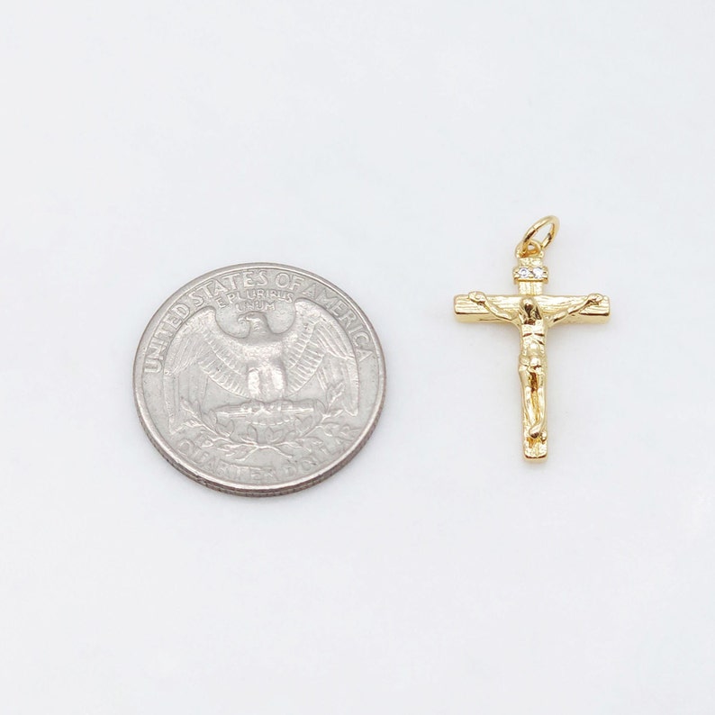 May include: A gold-tone crucifix pendant with a small clear stone at the top. The pendant is shown next to a US quarter for size comparison.