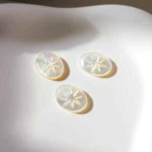 Peut inclure: Trois pendentifs ovales en nacre blanche avec un motif d'étoile.