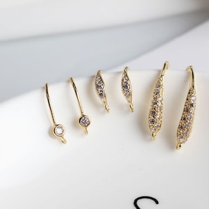 May include: Five gold earring findings with clear cubic zirconia stones. Two findings are curved and have a row of stones. Three findings are straight with a single stone at the end.