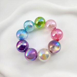 May include: A rainbow of iridescent glass beads, each with a different color, are arranged in a circle. The beads are all round and have a smooth, shiny finish.