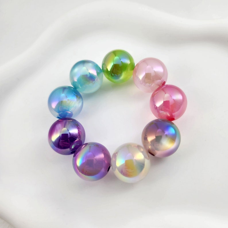 May include: A rainbow of iridescent glass beads, each with a different color, are arranged in a circle. The beads are all round and have a smooth, shiny finish.