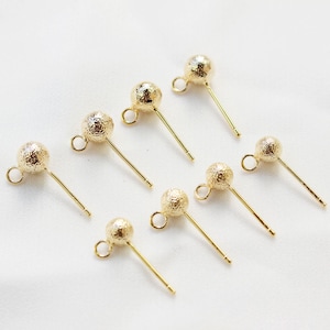 May include: Seven gold-toned earring posts with textured ball tops. The posts are straight and have a small loop at the top.
