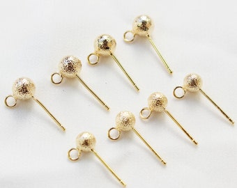 May include: Seven gold-toned earring posts with textured ball tops. The posts are straight and have a small loop at the top.