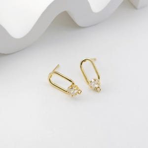 May include: A pair of gold-tone earrings with a rectangular shape and a cluster of clear cubic zirconia stones.