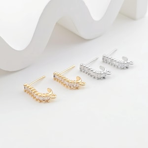 May include: Three pairs of earring findings with a curved bar design. Each bar is adorned with a row of clear cubic zirconia stones. The findings are available in gold, silver, and rhodium finishes.