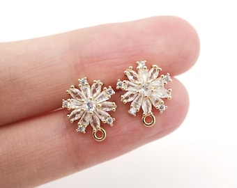 Könnte beinhalten: Ein Paar goldfarbene Ohrringe mit einem Schneeflocken-Design. Jeder Ohrring verfügt über einen Cluster aus klaren Zirkonia-Steinen, die in einer Schneeflockenform gefasst sind. Die Ohrringe haben eine Öse oben zum Anbringen an einer Halskette oder anderem Schmuck.