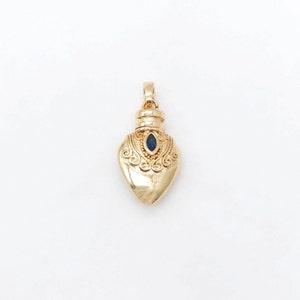 May include: A gold heart-shaped pendant with a blue gemstone in the center. The pendant has intricate details and a loop at the top for attaching to a chain.