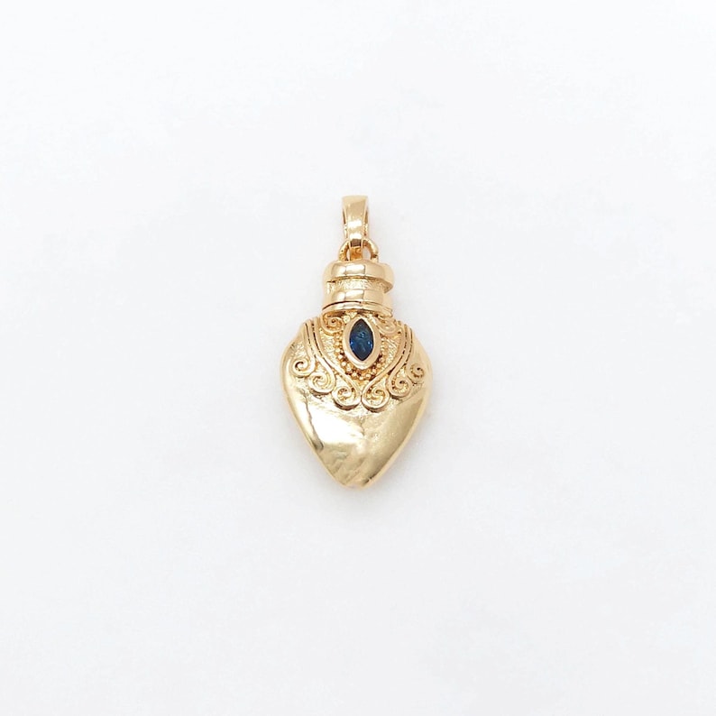 May include: A gold heart-shaped pendant with a blue gemstone in the center. The pendant has intricate details and a loop at the top for attaching to a chain.