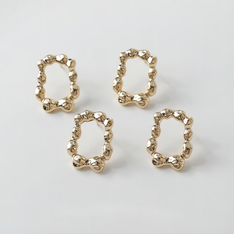 May include: Three gold-toned earrings with a textured, irregular oval shape. Each earring has a small, round hole at the top for attaching to a post.
