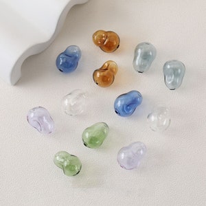 Può includere: Assortimento di 12 perline di vetro in vari colori, tra cui trasparente, azzurro, blu scuro, verde chiaro, verde scuro, lilla chiaro e marrone. Le perline hanno tutte la forma di una pera.