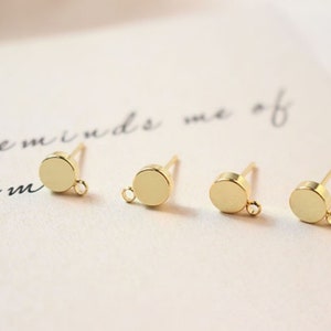 Op de afbeelding: Drie gouden oorbelsteentjes met een ronde schijf en een springring. De oorbelsteentjes liggen op een wit oppervlak.