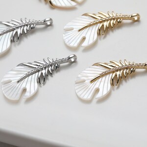 May include: Four white and gold feather-shaped pendants with a crystal-like design. The pendants are made of mother of pearl and have a gold or silver finish.