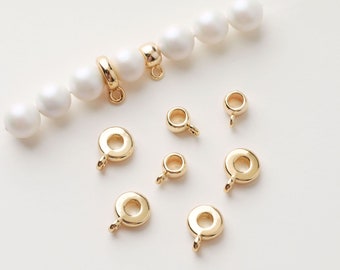 May include: Gold-toned metal bead caps with a small loop on the top. The bead caps are arranged on a white surface with a strand of white pearls.